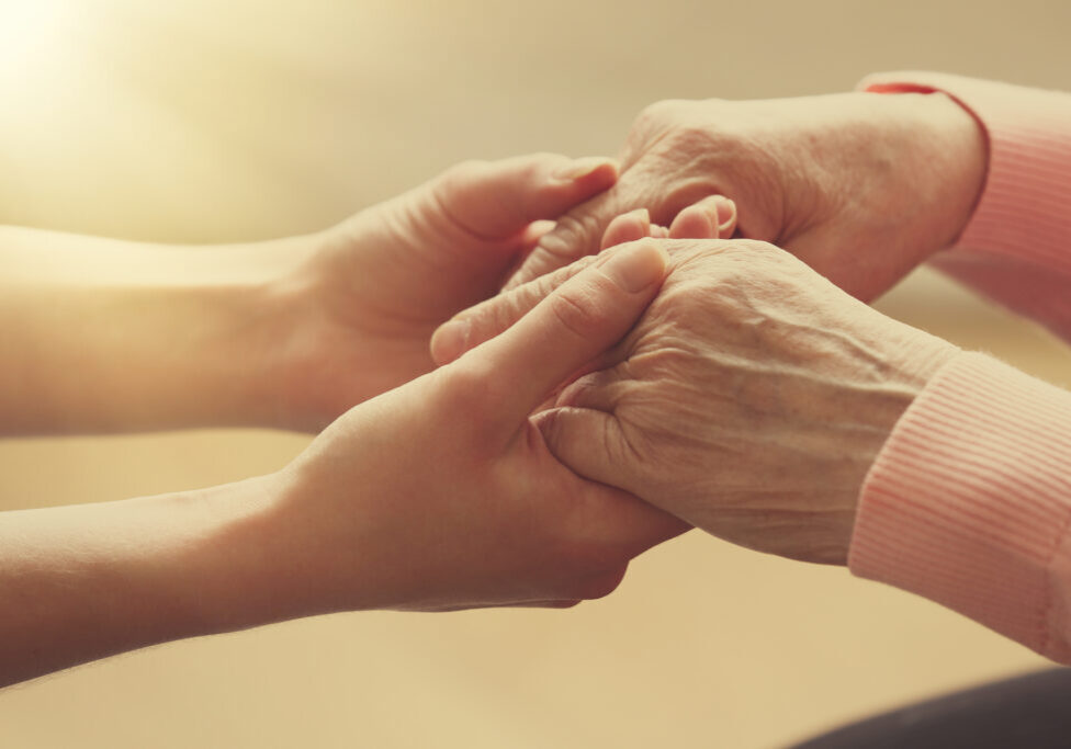 Old and young holding hands on light background, closeup